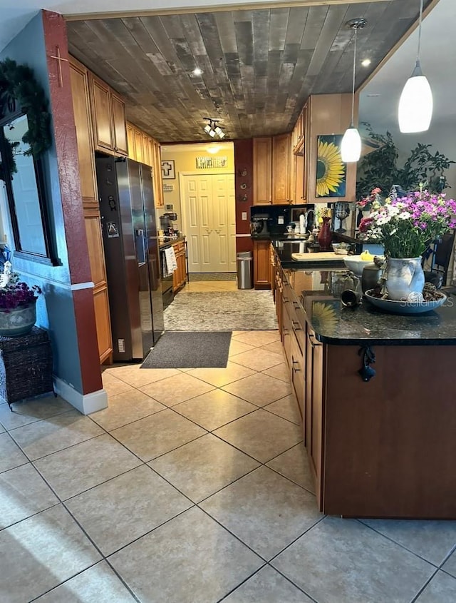 kitchen featuring dark countertops, stainless steel fridge, light tile patterned floors, and brown cabinetry
