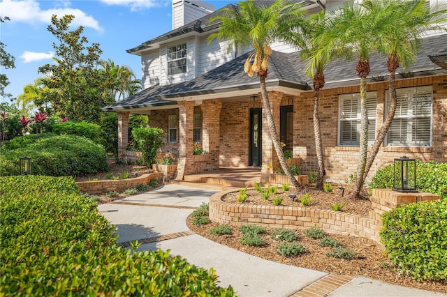 101 Ponce De Leon Blvd, Belleair, FL 33756 - view of front of home featuring a chimney, roof with shingles, brick siding, and covered porch