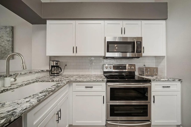 kitchen featuring stainless steel appliances, white cabinetry, a sink, and tasteful backsplash