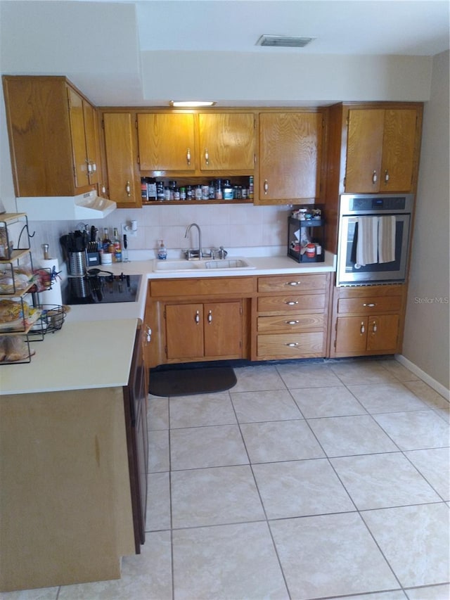 kitchen featuring tasteful backsplash, brown cabinets, a sink, light countertops, and oven