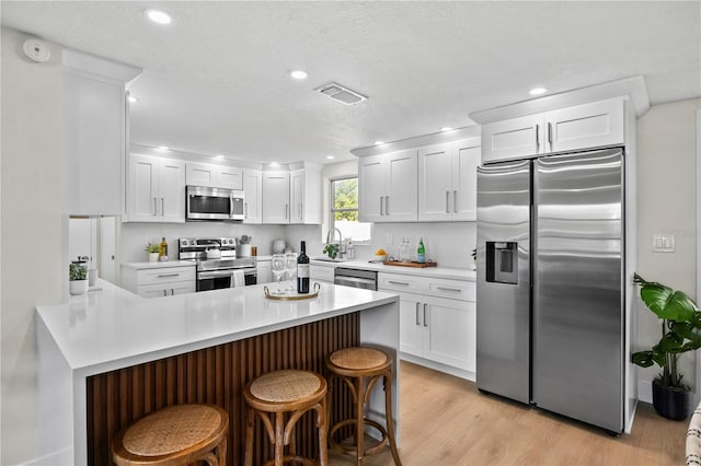 kitchen featuring light wood-style flooring, stainless steel appliances, recessed lighting, a peninsula, and visible vents