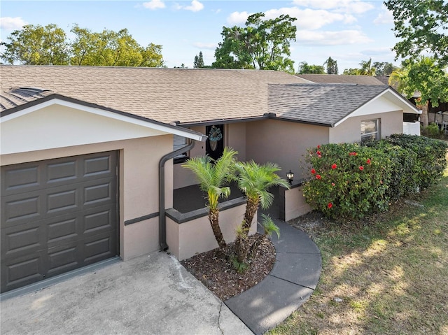 ranch-style home featuring concrete driveway, an attached garage, a shingled roof, and stucco siding
