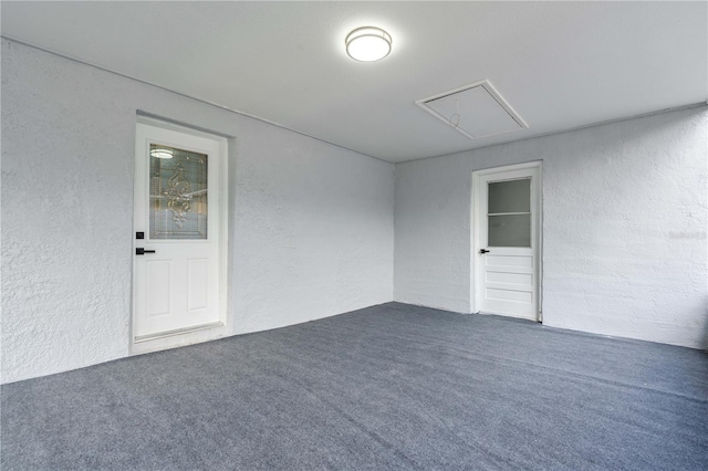 carpeted empty room with attic access and a textured wall