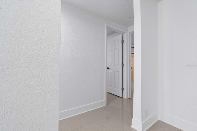corridor featuring baseboards and a textured wall