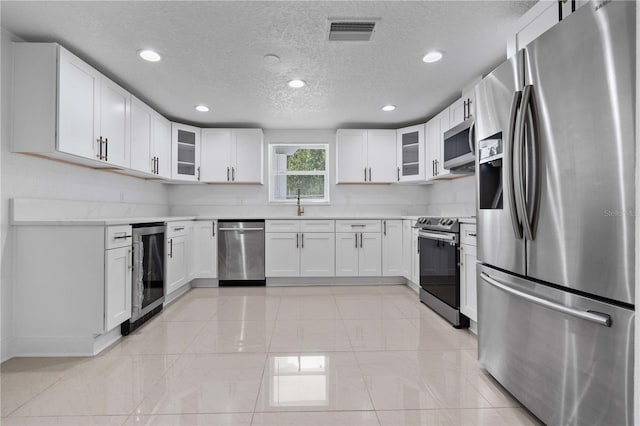 kitchen with appliances with stainless steel finishes, beverage cooler, a textured ceiling, recessed lighting, and visible vents