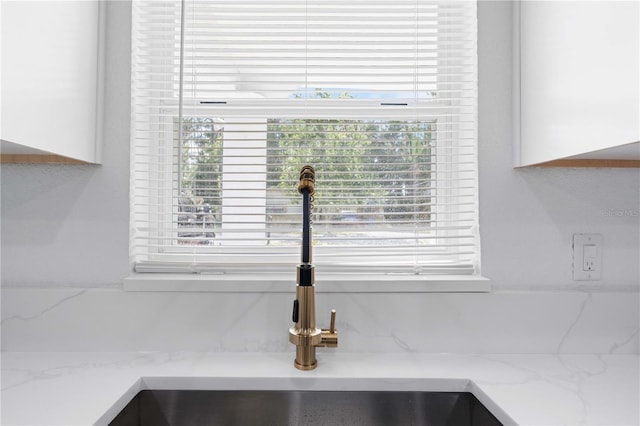 interior details featuring a sink, light stone countertops, and white cabinetry