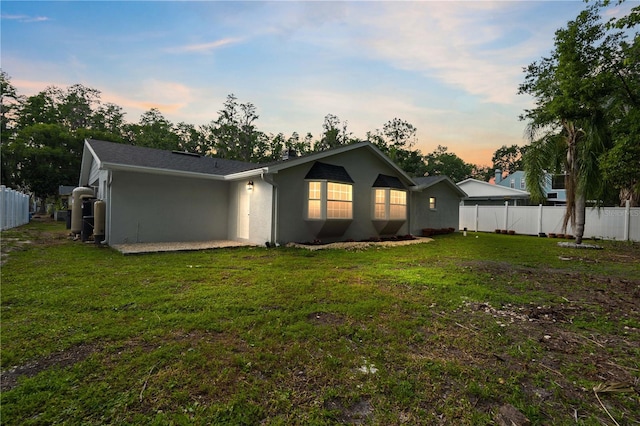 back of property at dusk featuring a lawn, fence, and stucco siding