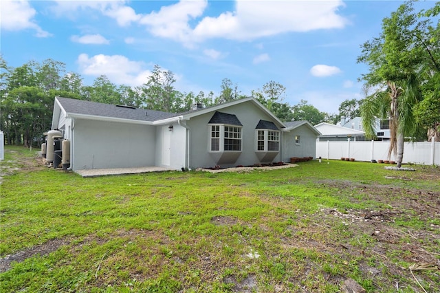 back of house featuring a yard, fence, and stucco siding