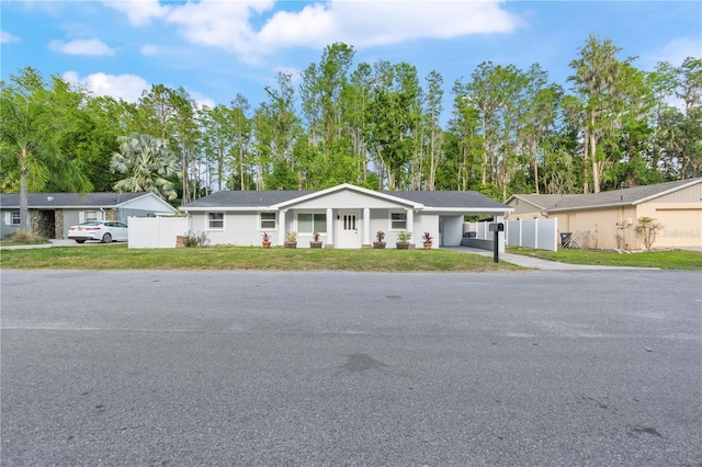 ranch-style house featuring a front lawn, fence, driveway, and an attached carport