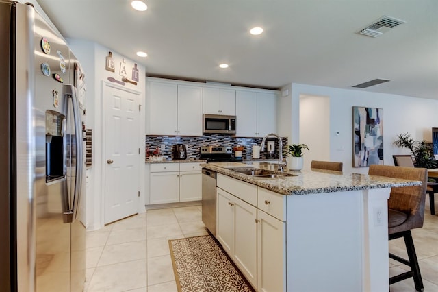 kitchen with visible vents, appliances with stainless steel finishes, tasteful backsplash, a sink, and a breakfast bar