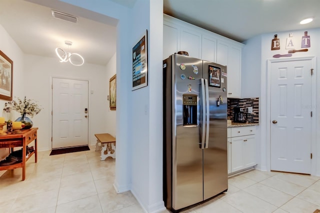 kitchen featuring backsplash, light stone countertops, light tile patterned floors, stainless steel fridge with ice dispenser, and white cabinets