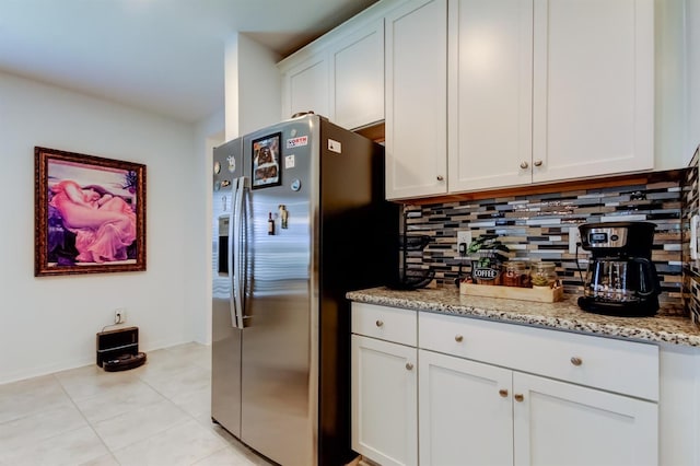 kitchen with backsplash, light stone countertops, white cabinets, stainless steel fridge, and light tile patterned flooring