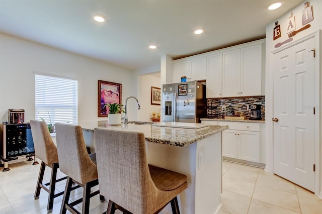kitchen featuring light tile patterned floors, tasteful backsplash, a breakfast bar area, and stainless steel refrigerator with ice dispenser