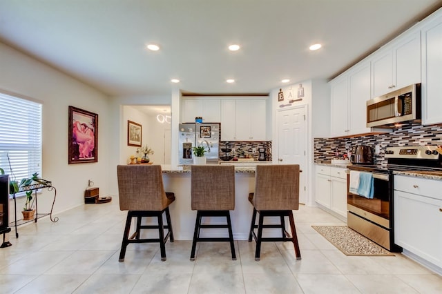 kitchen with white cabinets, stainless steel appliances, a kitchen bar, and tasteful backsplash