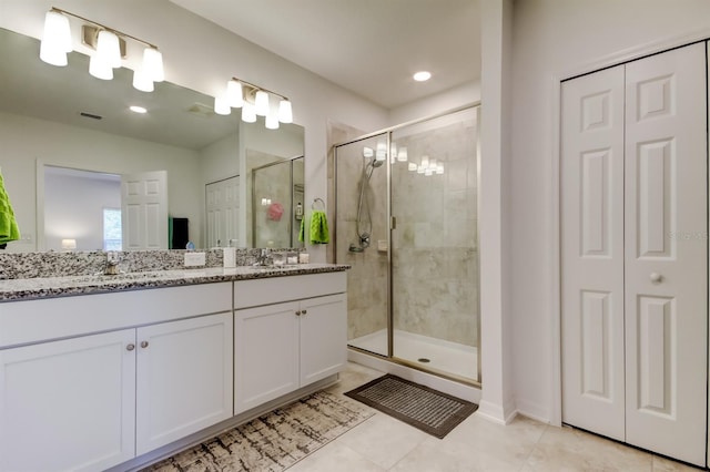 bathroom featuring a sink, tile patterned flooring, double vanity, a shower stall, and a closet
