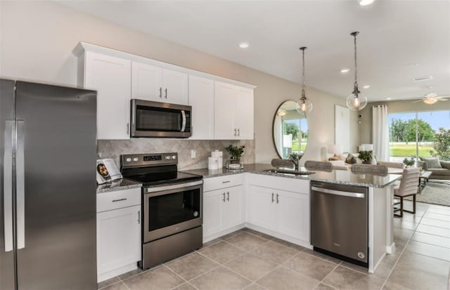 kitchen with a peninsula, open floor plan, dark stone countertops, backsplash, and stainless steel appliances