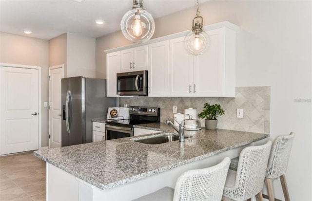 kitchen with decorative backsplash, a peninsula, light stone counters, a sink, and stainless steel appliances