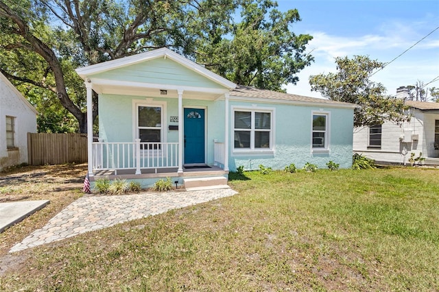 bungalow-style home with covered porch, fence, a front yard, and stucco siding