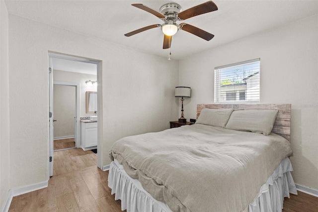bedroom with baseboards, a ceiling fan, ensuite bath, and wood finished floors
