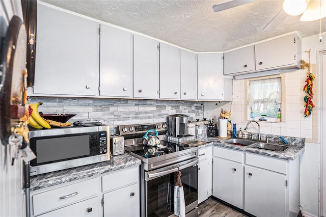 kitchen with appliances with stainless steel finishes, a sink, a textured ceiling, wood finished floors, and tasteful backsplash