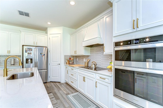 kitchen with visible vents, premium range hood, white cabinets, a sink, and stainless steel appliances