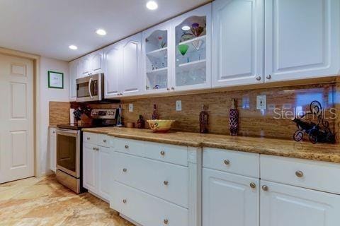 kitchen with decorative backsplash, glass insert cabinets, recessed lighting, white cabinetry, and stainless steel appliances