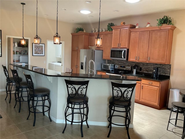 kitchen featuring appliances with stainless steel finishes, a kitchen breakfast bar, decorative backsplash, and washer and clothes dryer