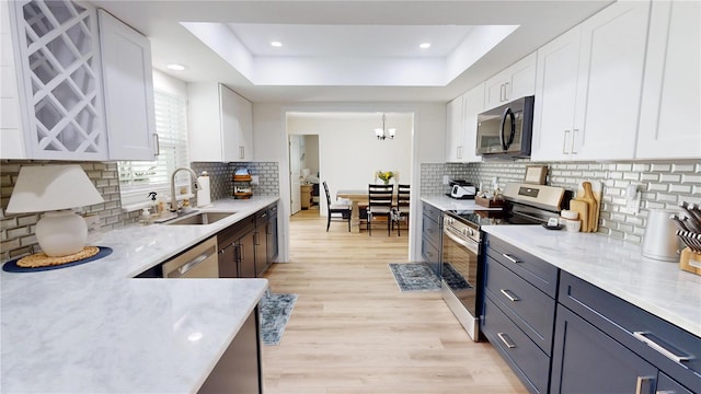 1849 Del Robles Dr, Clearwater, FL 33764 - kitchen featuring white cabinets, a sink, stainless steel appliances, backsplash, and a tray ceiling