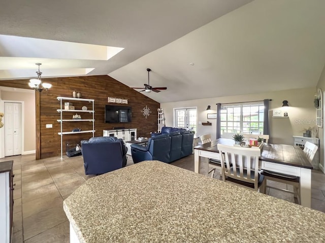 tiled dining area featuring lofted ceiling with skylight, ceiling fan, and wooden walls