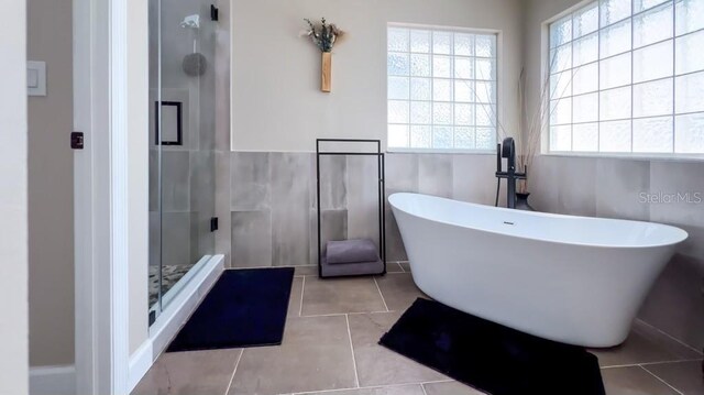 full bath featuring tile patterned flooring, a freestanding tub, a stall shower, and tile walls