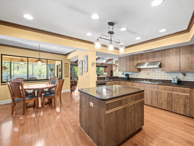 kitchen with plenty of natural light, crown molding, a center island, tasteful backsplash, and under cabinet range hood