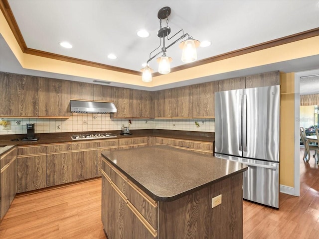 kitchen with dark countertops, gas cooktop, freestanding refrigerator, decorative backsplash, and under cabinet range hood