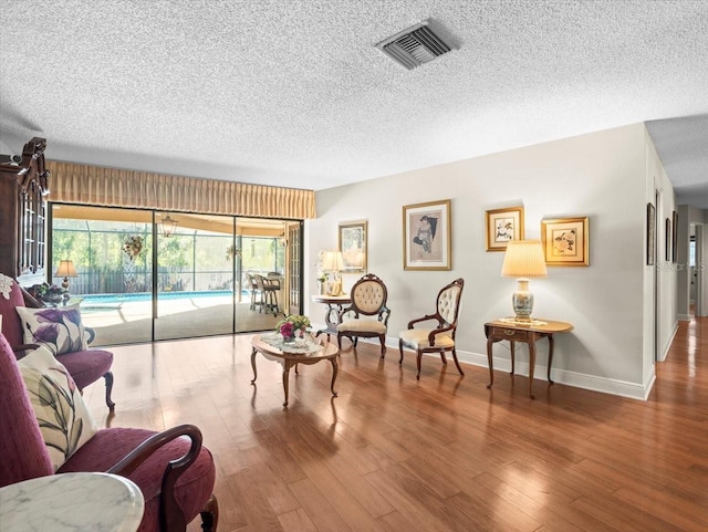 living area with wood finished floors, a wealth of natural light, a textured ceiling, and visible vents