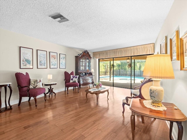 sitting room featuring visible vents, a textured ceiling, and wood finished floors
