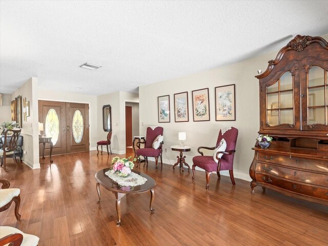 living area with wood finished floors, baseboards, a textured ceiling, and visible vents
