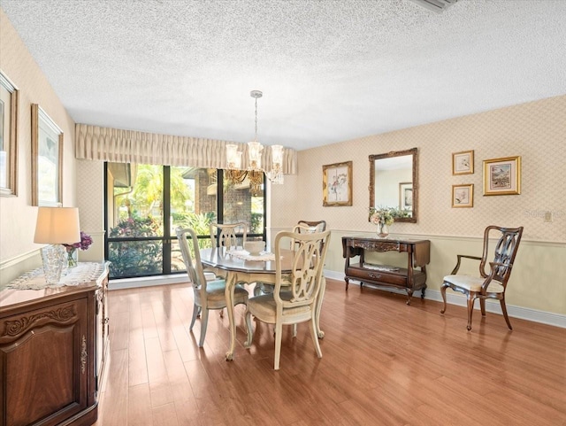 dining area featuring a textured ceiling, wood finished floors, a chandelier, and wallpapered walls