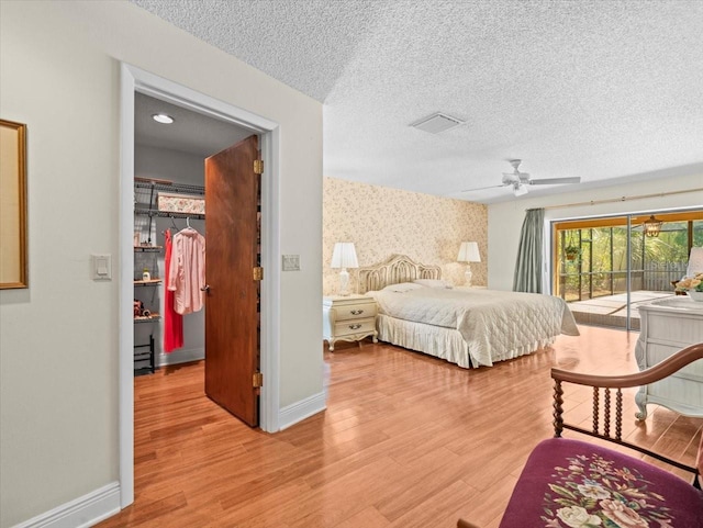 bedroom with light wood-style floors, a textured ceiling, access to exterior, wallpapered walls, and a spacious closet