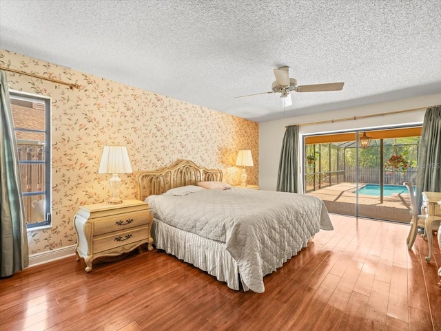 bedroom with access to outside, a textured ceiling, baseboards, wallpapered walls, and wood finished floors