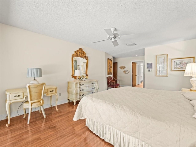 bedroom with ceiling fan, light wood finished floors, a textured ceiling, baseboards, and visible vents