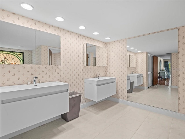 bathroom with baseboards, recessed lighting, two vanities, and wallpapered walls