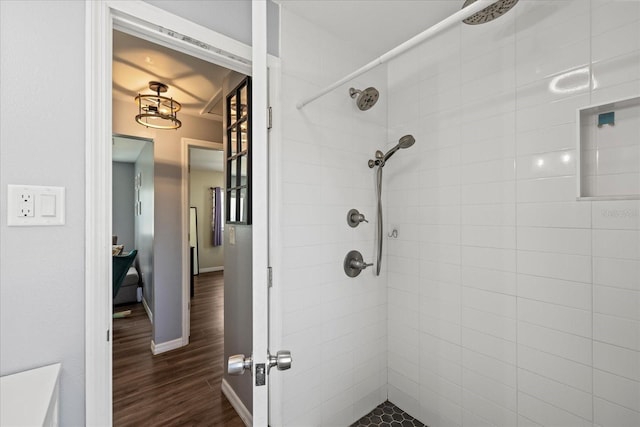 bathroom with baseboards, wood finished floors, and tiled shower