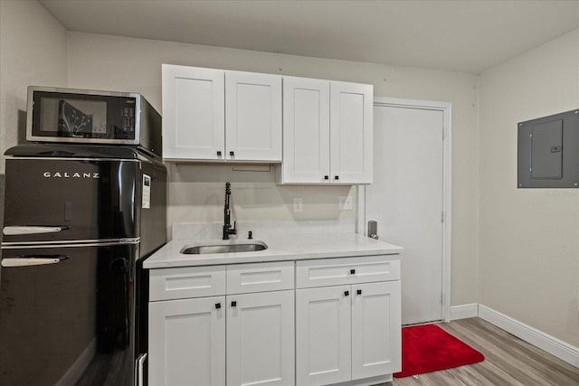 kitchen featuring electric panel, refrigerator, wood finished floors, a sink, and white cabinets