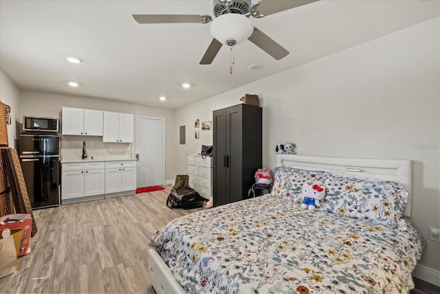 bedroom featuring a sink, baseboards, light wood-style floors, and black refrigerator