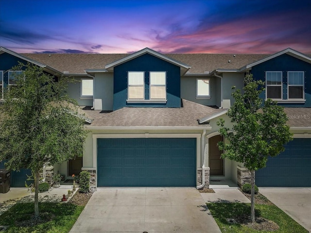 view of front facade with an attached garage, driveway, stone siding, and stucco siding