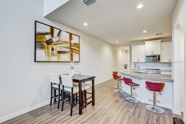 kitchen with stainless steel microwave, a breakfast bar, light wood finished floors, and visible vents