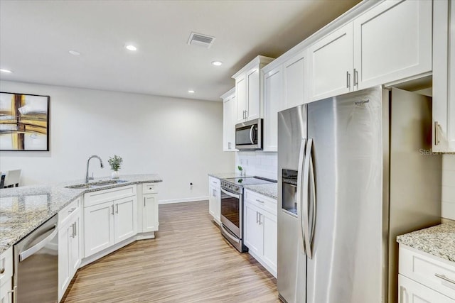 kitchen with a sink, stainless steel appliances, white cabinetry, light wood-type flooring, and visible vents