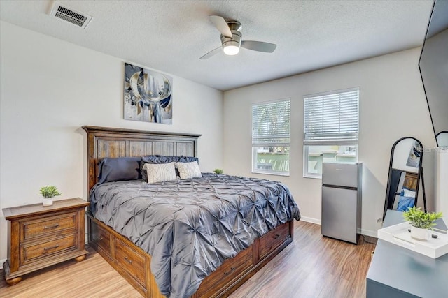 bedroom featuring a textured ceiling, visible vents, baseboards, freestanding refrigerator, and light wood-style floors