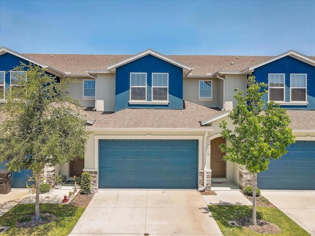 view of front of house with a garage, stone siding, stucco siding, a shingled roof, and driveway