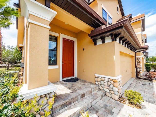 doorway to property with an attached garage, stucco siding, and stone siding