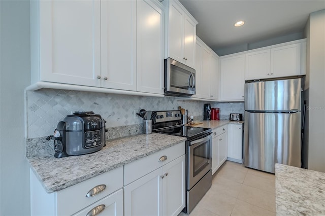 kitchen featuring white cabinets, light stone counters, appliances with stainless steel finishes, light tile patterned floors, and tasteful backsplash